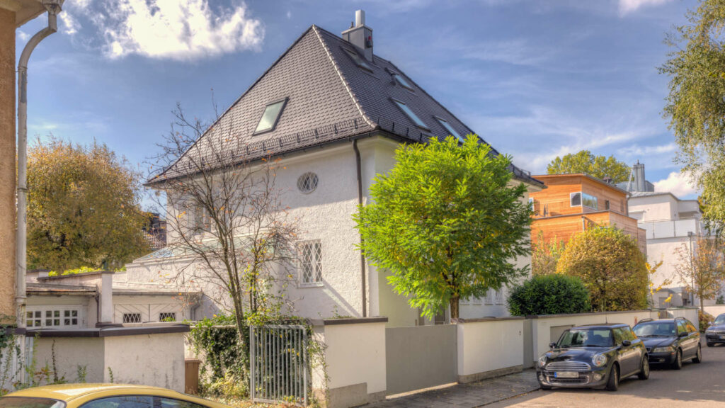 Freistehendes weißes Einfamilienhaus mit spitzem Satteldach in einer Münchner Wohnstraße