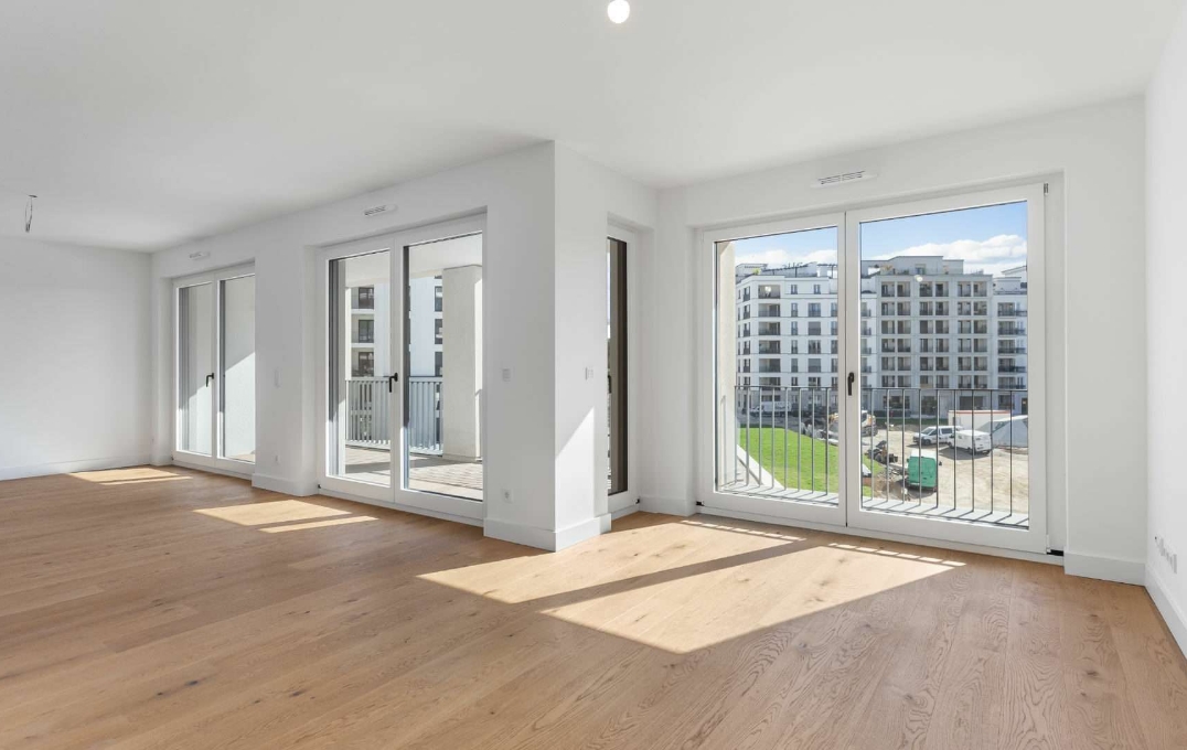 Leeres helles Wohnzimmer mit bodentiefen Fenstern und Parkett in einer Neubauwohnung am Nockherberg