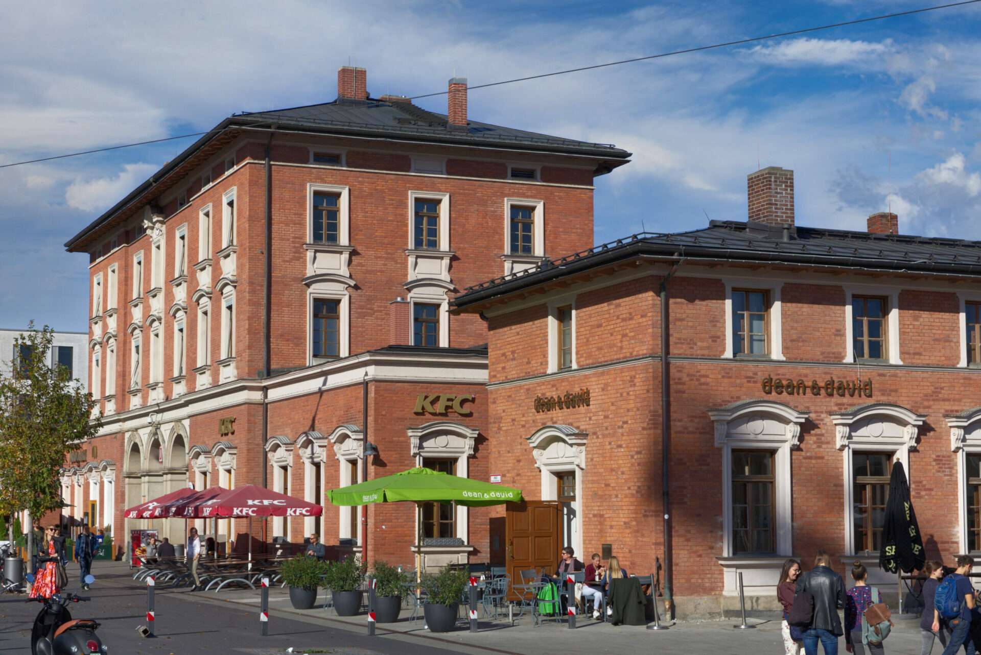 Historisches Backsteingebäude des Bahnhofs Pasing Südseite mit Außenbestuhlung eines Straßencafés in München