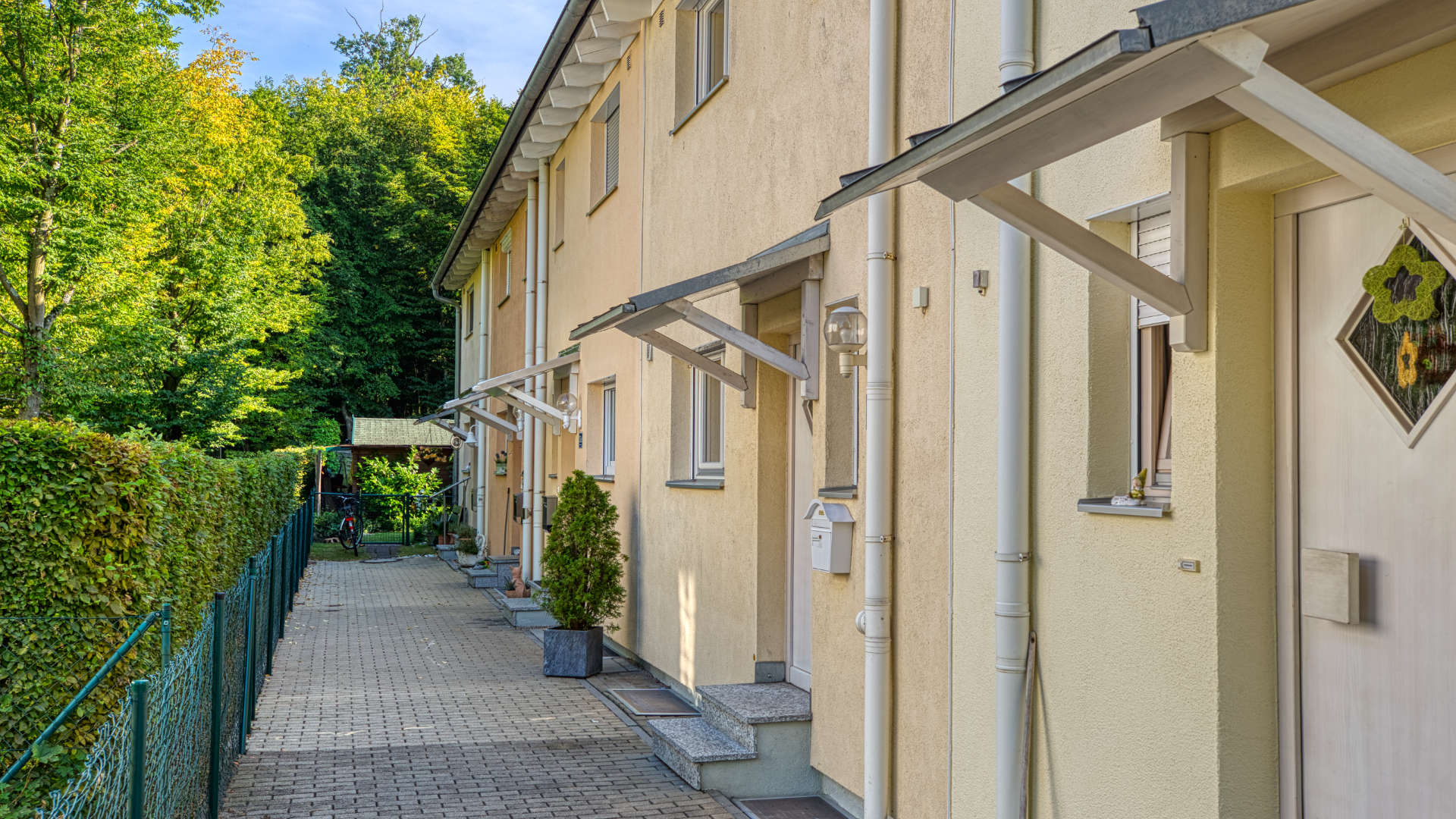 Gelbe Reihenhauszeile mit gepflastertem Weg und grüner Hecke in Germering bei München
