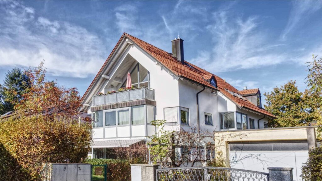 Weißes Einfamilienhaus mit rotem Satteldach und herbstlich gefärbten Bäumen