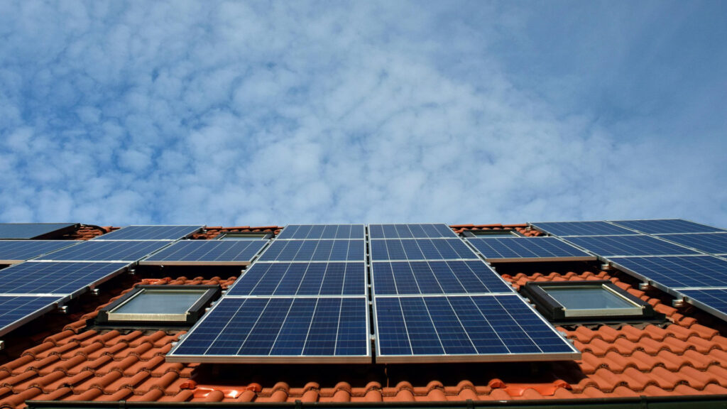 Photovoltaikanlage mit Dachfenstern auf einem roten Ziegeldach vor blauem Himmel
