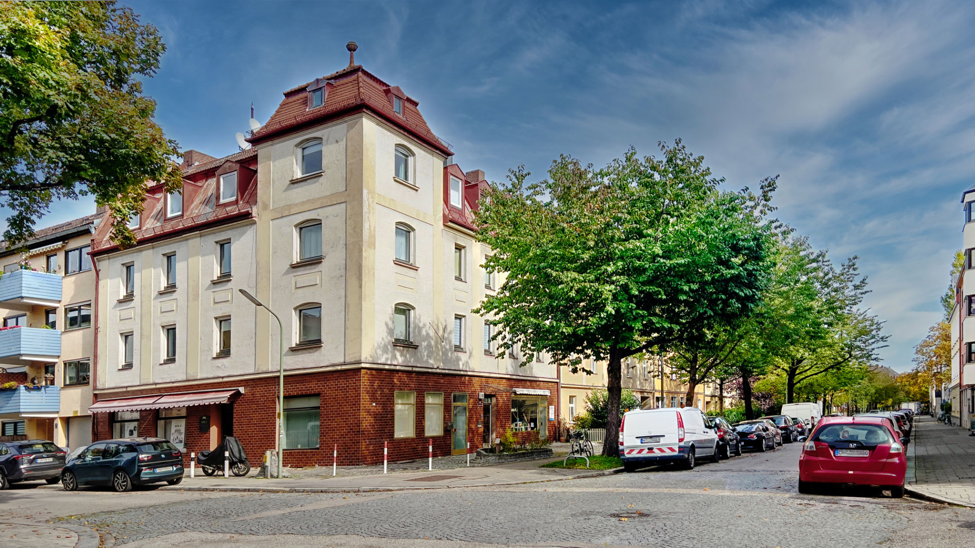 Historisches Eckhaus mit rotem Dach an einer Straßenkreuzung im Münchner Stadtteil Milbertshofen
