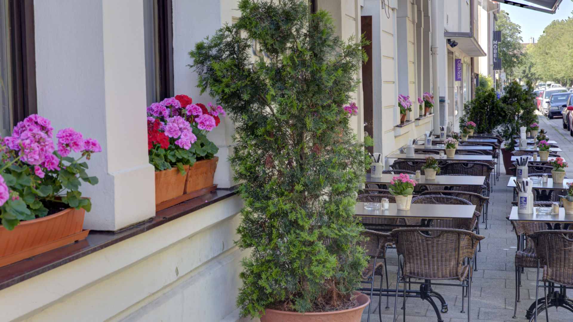 Gemütliches Straßencafé mit pinken Blumenkästen und Sitzplätzen im Münchner Stadtteil Milbertshofen