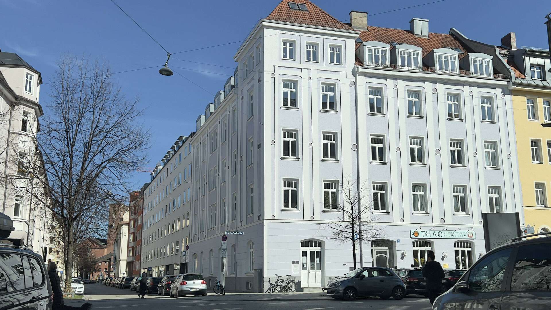 Weißes Altbau-Eckhaus mit gelbem Nachbargebäude an einer Straßenkreuzung im Münchner Stadtteil Au