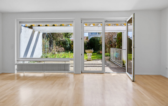 Leeres Wohnzimmer mit Parkettboden und Terrassentür zum Garten im Reihenendhaus in Unterhaching zur Miete