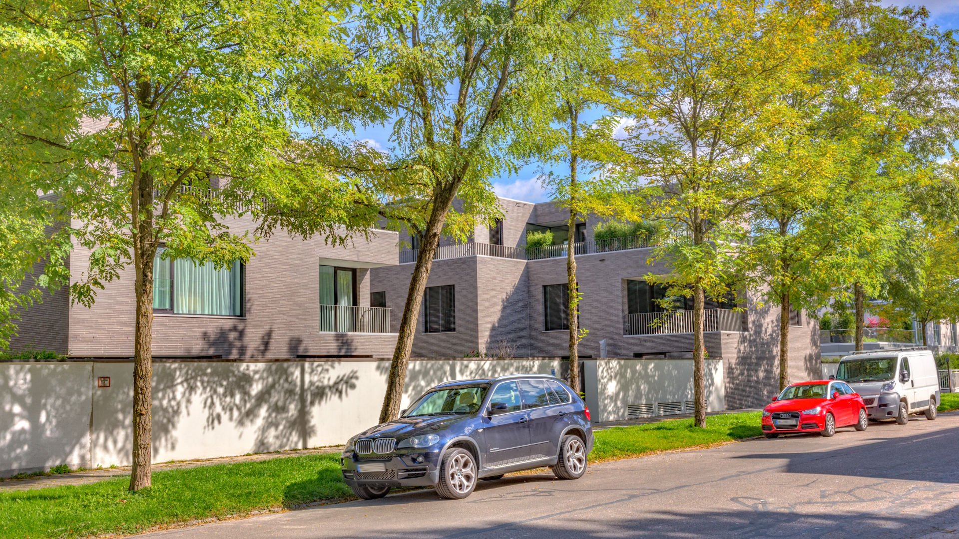 Moderne Steinfassaden-Villen mit Bäumen und parkenden Autos im Münchner Stadtteil Bogenhausen