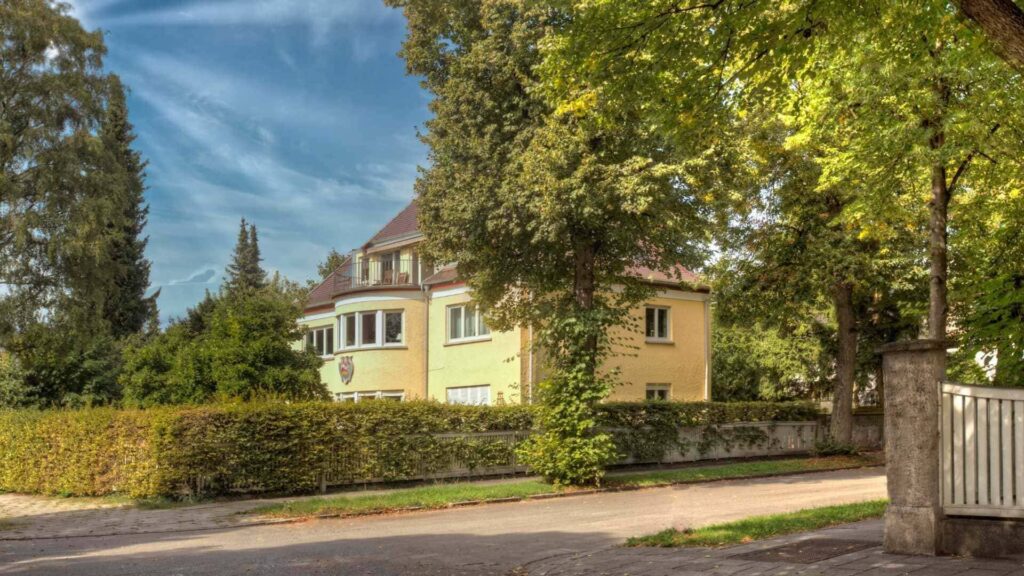 Gelbe historische Villa zwischen hohen Bäumen an einer ruhigen Straße