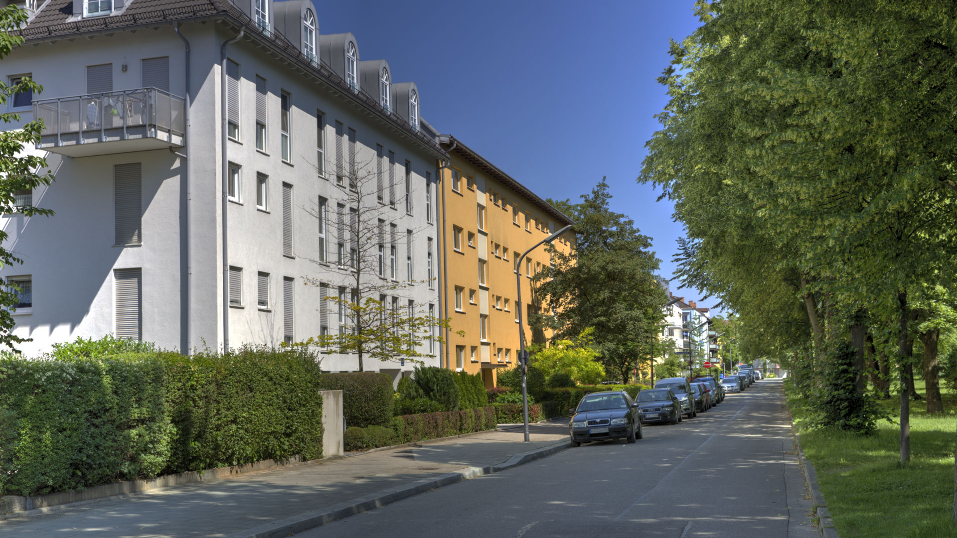 Mehrstöckige Wohnhäuser entlang einer baumbestandenen Straße im Münchner Stadtteil Milbertshofen