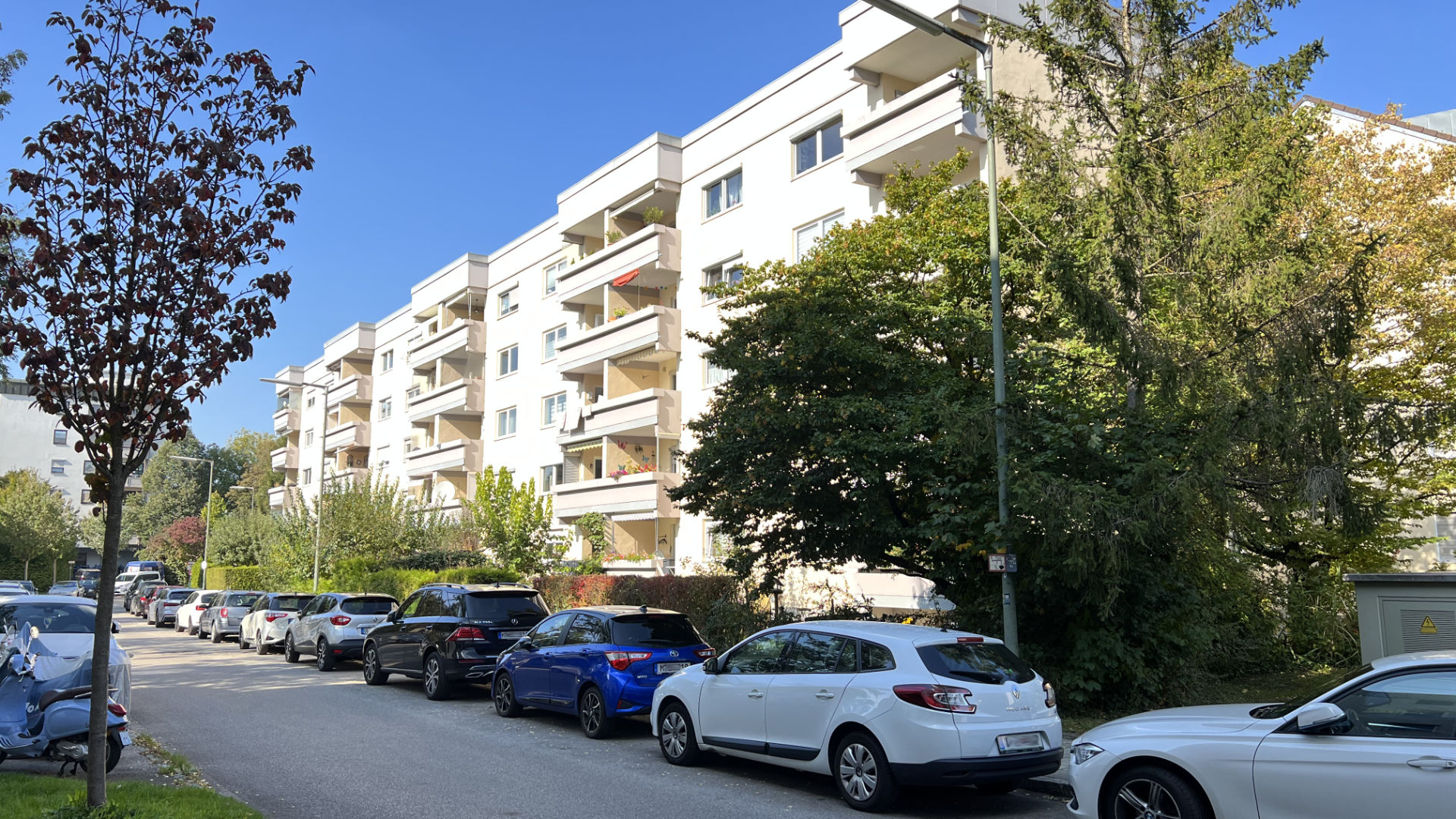 Weißes mehrstöckiges Wohnhaus mit Balkonen an einer baumbestandenen Straße in München-Untermenzing