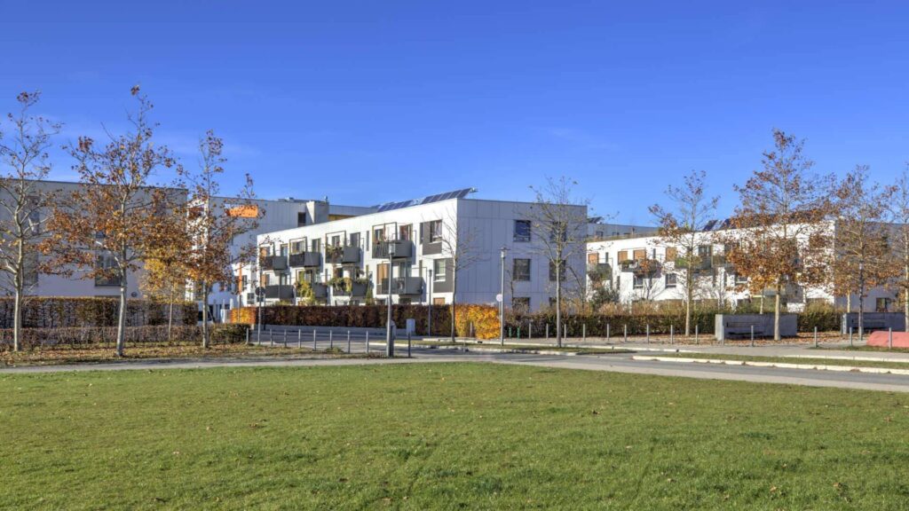 Modernes Mehrfamilienhaus mit weißer Fassade und großer Rasenfläche im Herbst in München