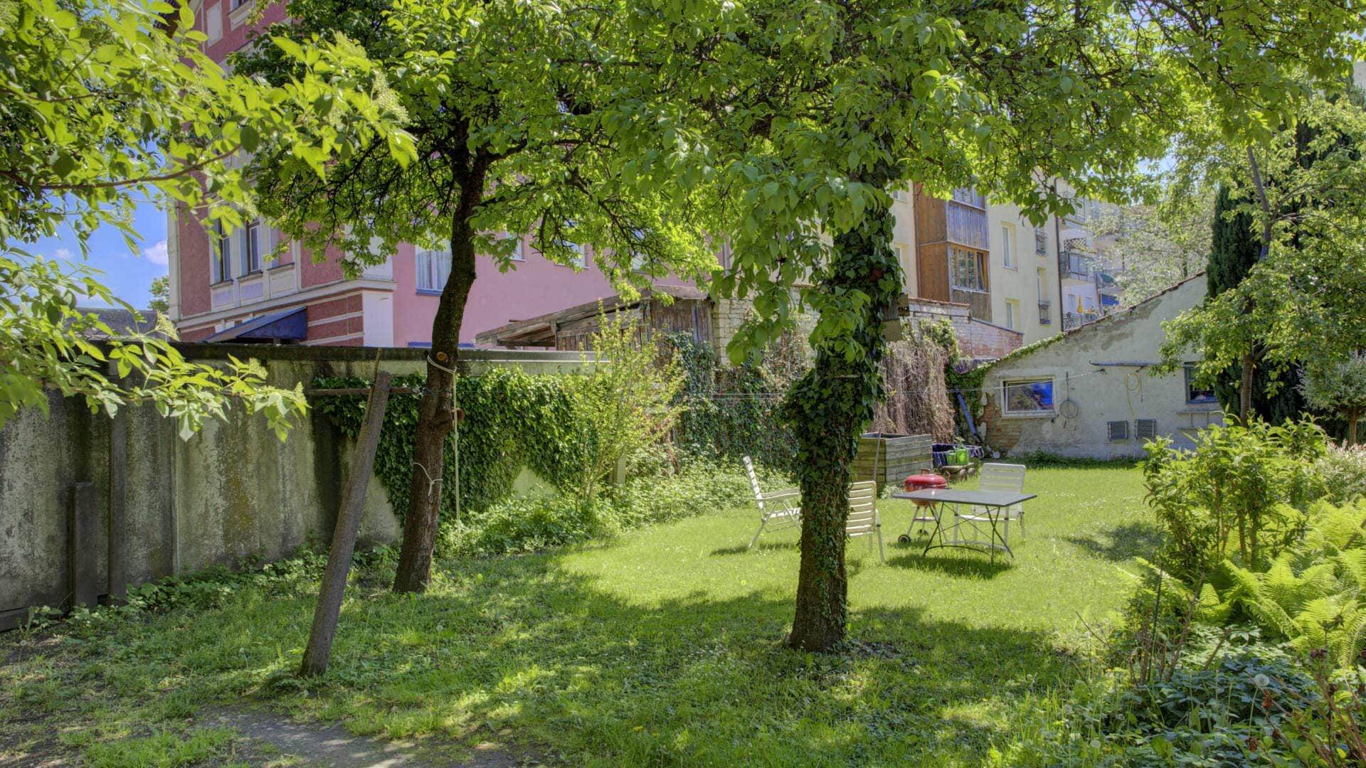 Begrünter Garten mit Bäumen, Sitzgruppe und Mauer als Sichtschutz auf einem Grundstück in Rosenheim.