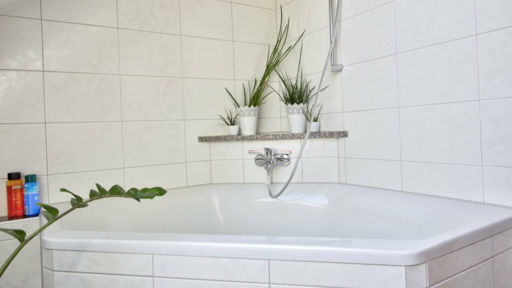 Weiße Eckbadewanne mit gefliester Wand und kleinen Pflanzen in einer Wohnung in Aubing