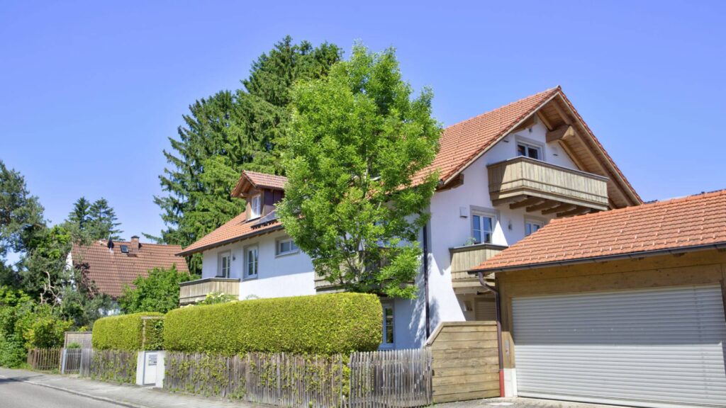 Weißes Mehrfamilienhaus mit Ziegeldach von der Straße aus gesehen in Aubing München