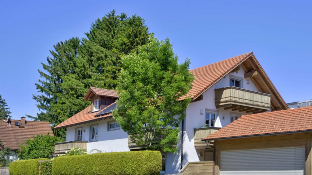Wohnhaus mit Satteldach und Balkon hinter grünem Baum in Aubing München