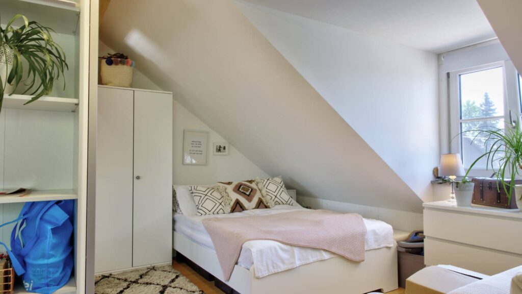 Schlafbereich mit Doppelbett unter Dachschräge und Fenster in einer Dachgeschosswohnung in Aubing