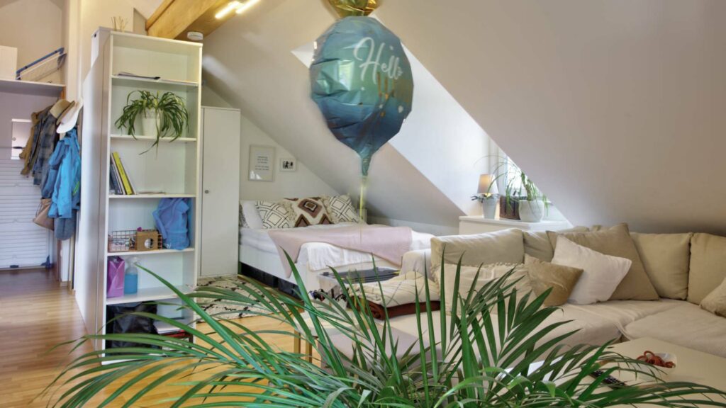 Kombinierter Schlaf- und Wohnbereich mit Bett, Sofa und Dachschräge in einer Dachgeschosswohnung in Aubing
