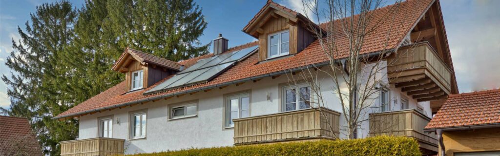 Exterior view of a house with a red tiled roof, wooden balconies, and hedge in Munich-Aubing.