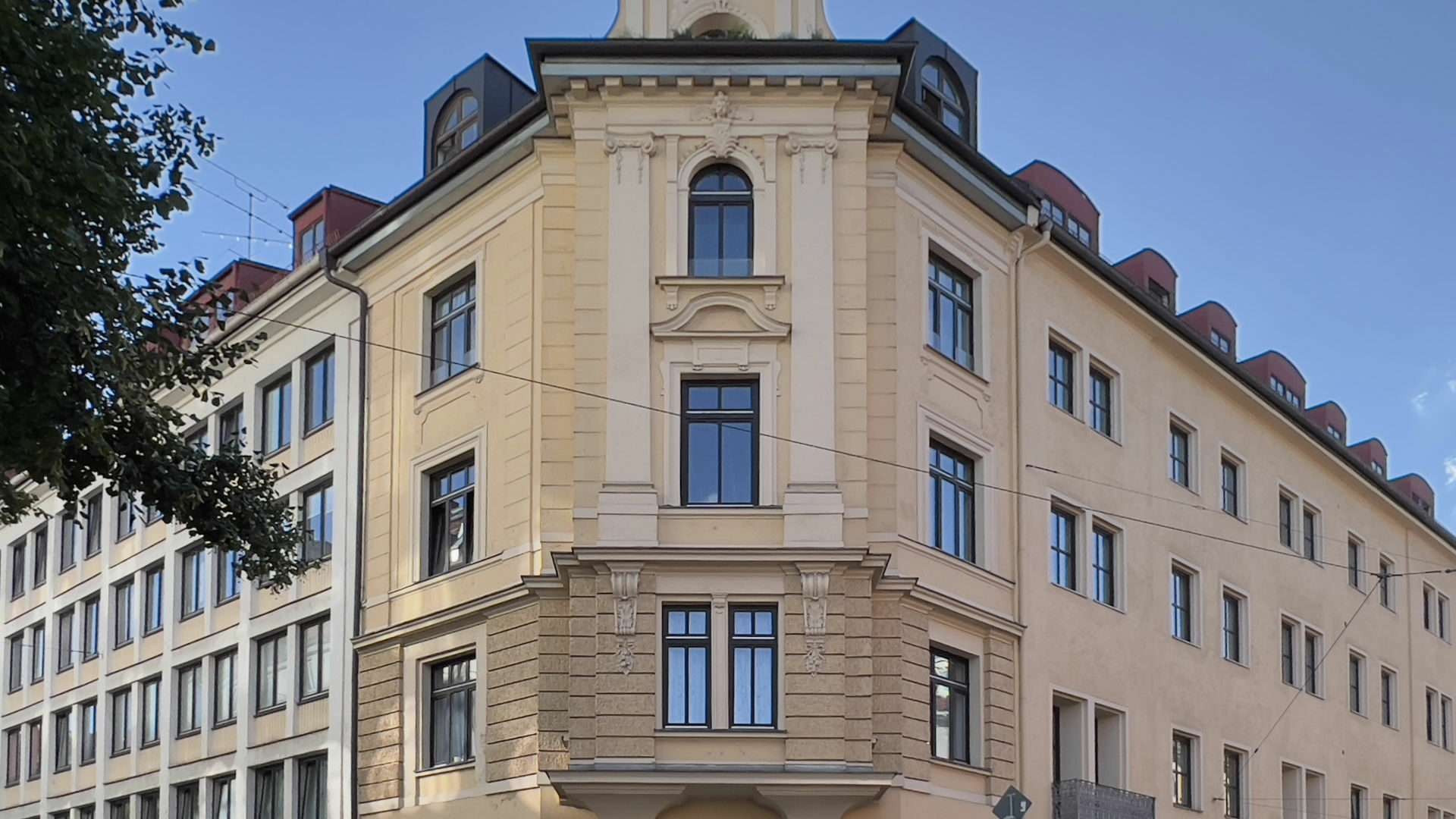Cremefarbenes Altbau-Eckhaus mit Säulen und rundem Erker in München