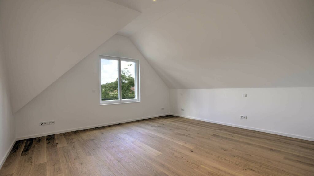 Leeres Dachgeschosszimmer mit Dachschräge, Fenster und Parkettboden in einer Doppelhaushälfte in Bogenhausen