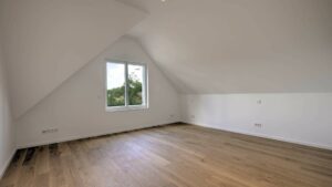 Leeres Dachgeschosszimmer mit Dachschräge, Fenster und Parkettboden in einer Doppelhaushälfte in Bogenhausen