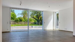 Leeres, helles Wohnzimmer mit Fliesenboden und großer Terrassentür zum Garten in einer Doppelhaushälfte in Bogenhausen