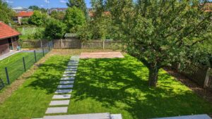 Großzügige Rasenfläche mit altem Baum, Steinweg und eingezäuntem Grundstück hinter einer Doppelhaushälfte in Bogenhausen