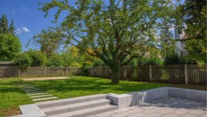 Weitläufiger Garten mit altem Baum, gepflasterter Terrasse und Sitzstufen hinter einer Doppelhaushälfte in Bogenhausen