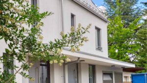 Detailansicht der weißen Hausfassade mit blühendem Strauch und Terrassenüberdachung einer Doppelhaushälfte in Bogenhausen