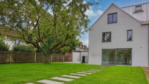 Weißes Wohnhaus mit Satteldach, großer Fensterfront und gepflegtem Rasen mit Trittplatten in Bogenhausen