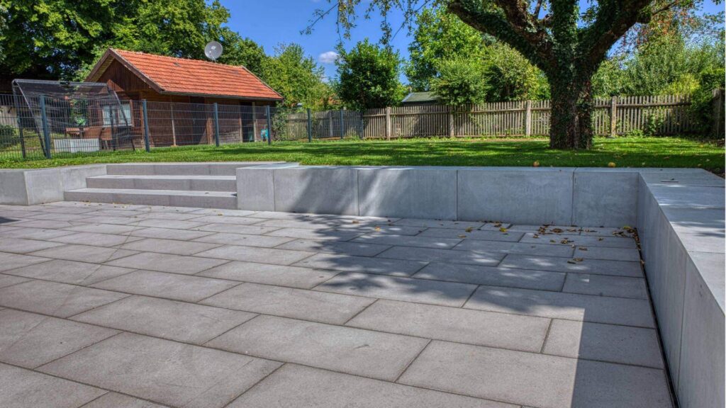 Gepflasterte Terrasse mit Sitzstufen und Blick auf ein Gartenhaus und alten Baum in Bogenhausen