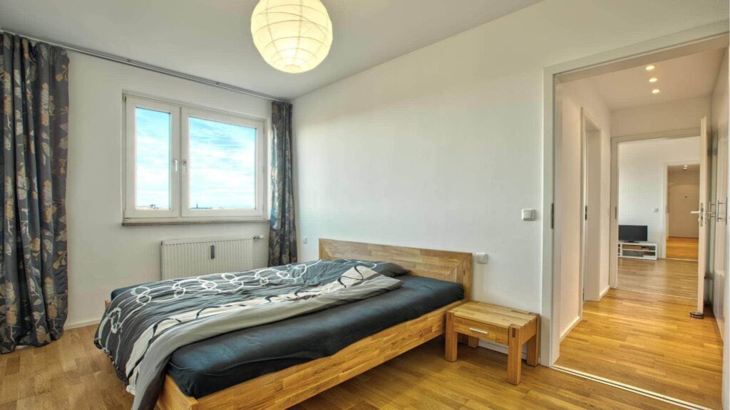 Bewohntes Schlafzimmer mit Holzbett, Nachttisch und Blick in den Flur in einer Wohnung in Bogenhausen.