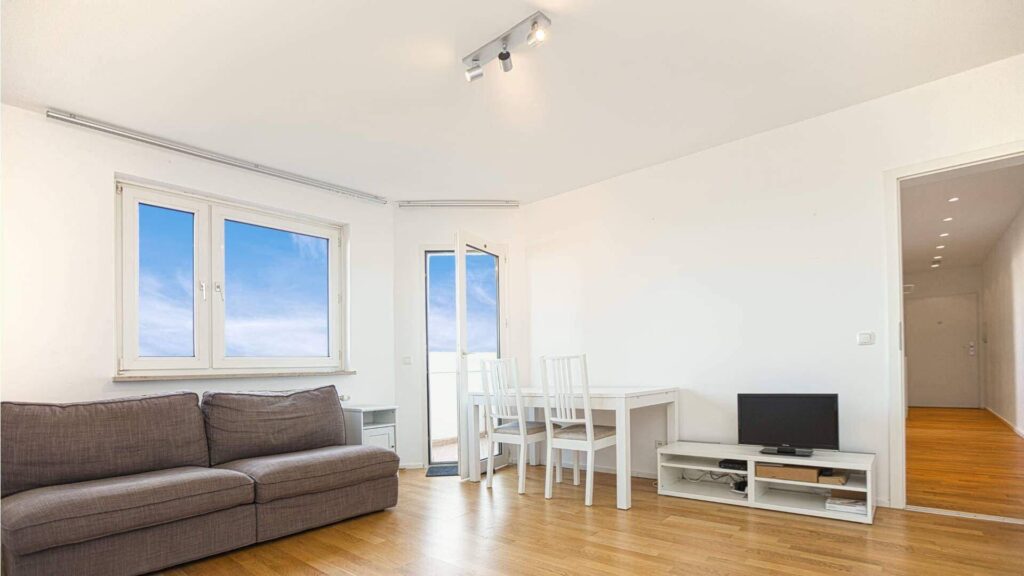 Helles Wohnzimmer mit grauer Couch, Essbereich und Fenster mit Himmelsblick in Bogenhausen.