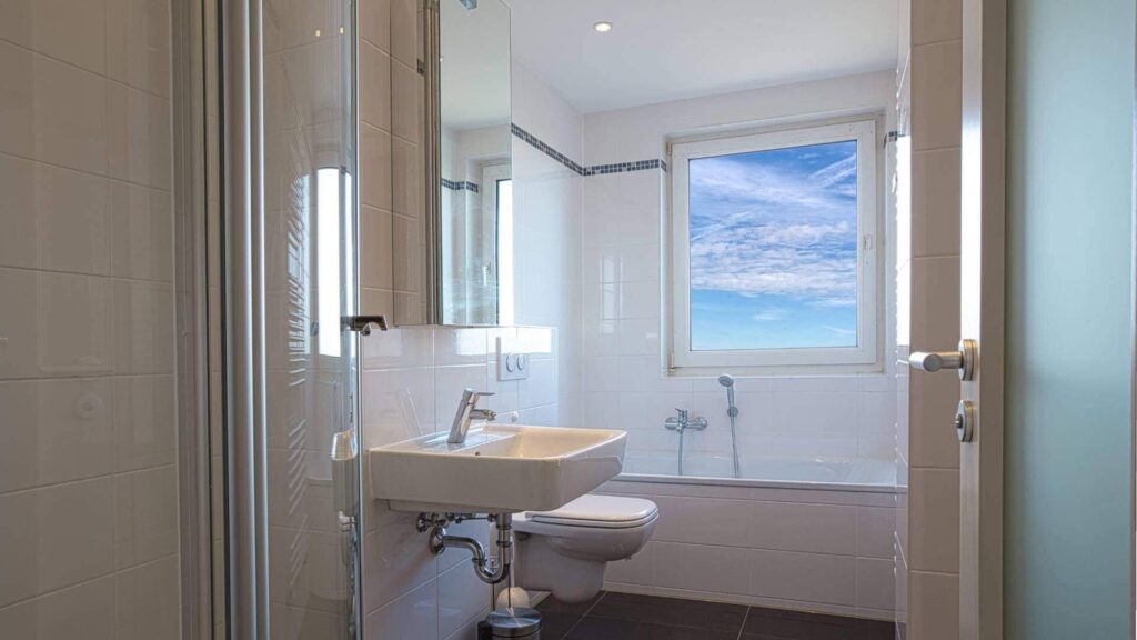 Badezimmer mit Wanne, Waschbecken, Fenster mit Himmelsblick und dunklem Boden in einer Wohnung in Bogenhausen.