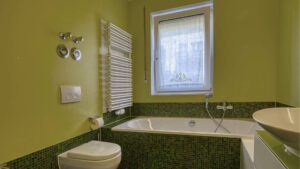 Badezimmer mit grün gefliester Badewanne, WC und Fenster in einer Wohnung in Bogenhausen