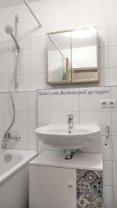 Bathroom of the apartment in Munich-Bogenhausen with white tiles, washbasin and mirrored cabinet