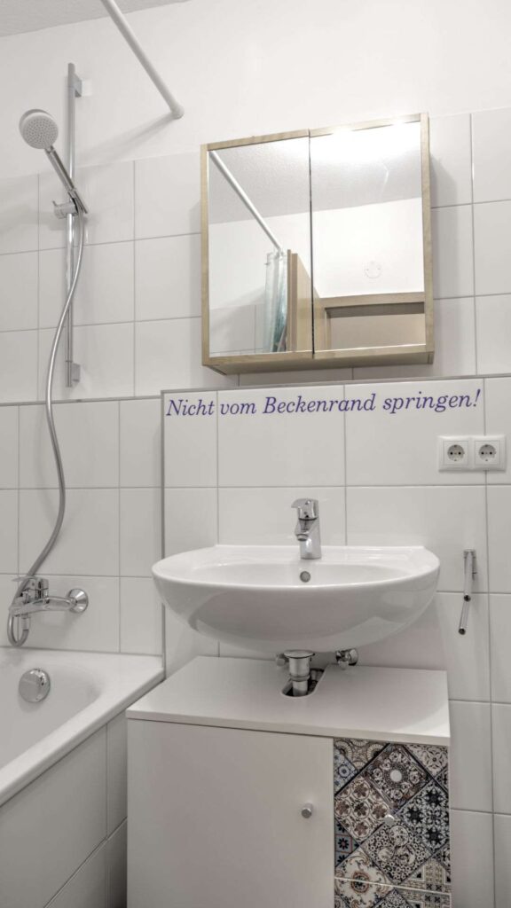 Bathroom of the apartment in Munich-Bogenhausen with white tiles, washbasin and mirrored cabinet