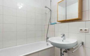 Tiled bathroom of the Bogenhausen apartment with bathtub, sink, and mirrored cabinet