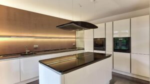 Elegante weiße Küche mit Kochinsel, Dunstabzugshaube und Holzpaneel-Rückwand in einer Wohnung in Bogenhausen