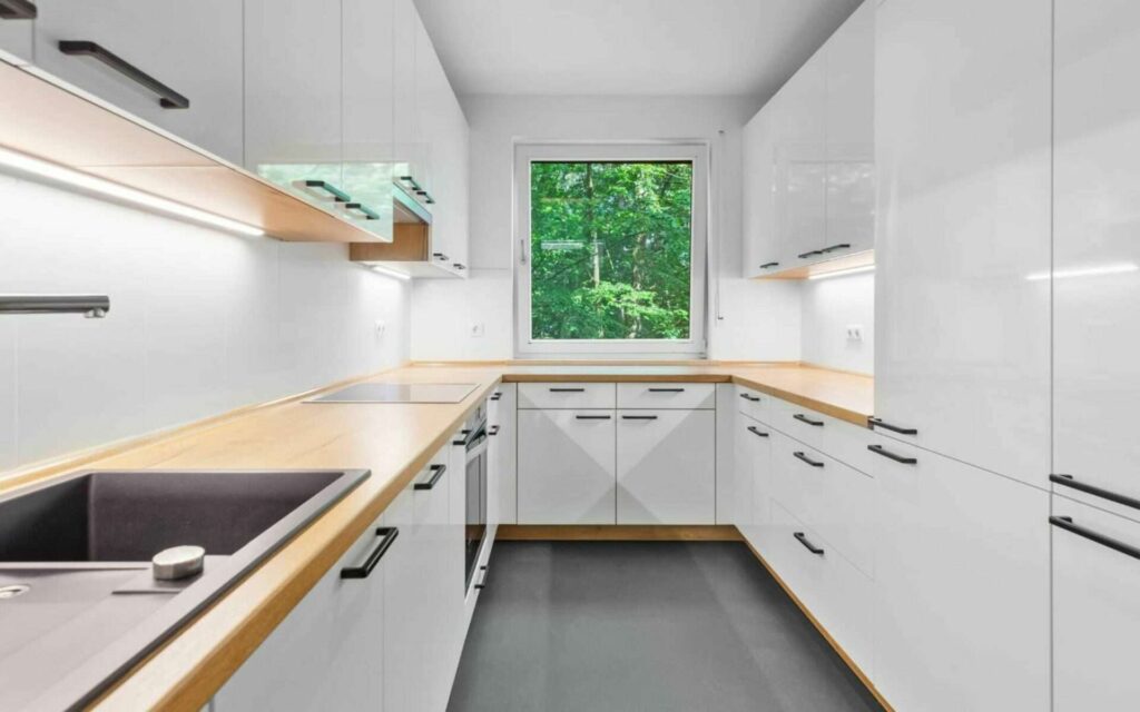 Narrow white fitted kitchen of the Bogenhausen apartment with a window at the end of the room