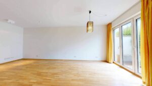 Unmöbliertes Wohnzimmer mit Parkettboden und Terrassentür mit gelben Vorhängen in einer Wohnung in Bogenhausen