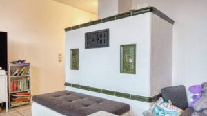 White tiled stove with a green decorative trim and built-in bench in a lived-in living room with a bookshelf.