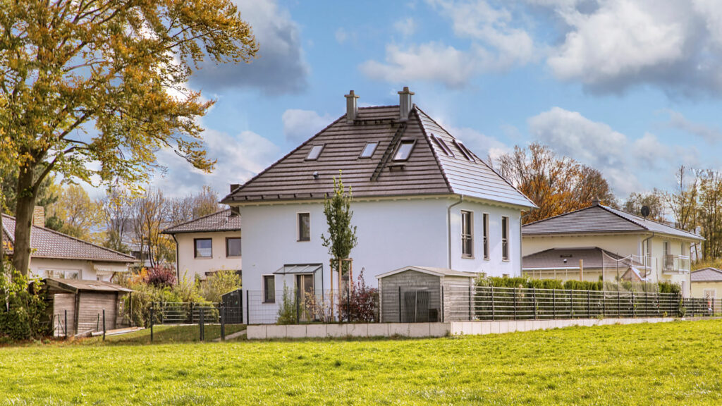 Weißes Haus mit dunklem Dach und grüner Wiese im Herbst