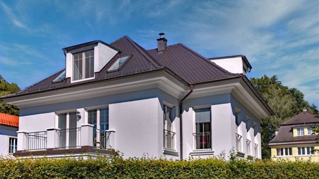 Weiße Villa mit Dachgaube, dunklem Ziegeldach und Hecke – Beispielbild zum Thema Eigentumswohnung kaufen in München
