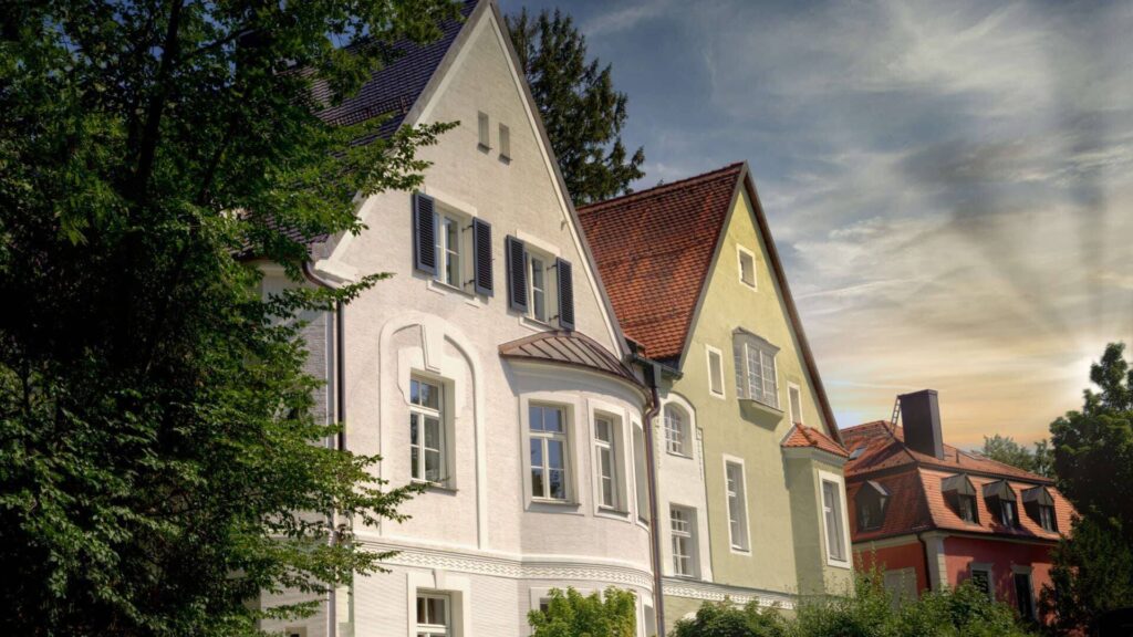Weißes und gelbgrünes Giebelhaus nebeneinander in der Abenddämmerung – Symbolbild zum Energieausweis beim Immobilienverkauf