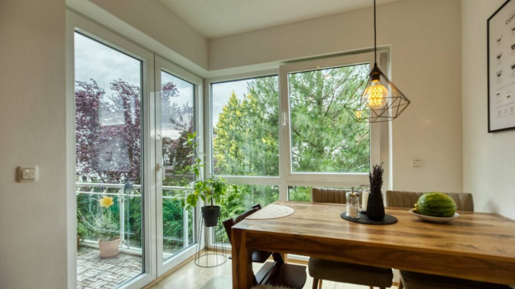 Dining area with a wooden table, pendant light, and large floor-to-ceiling windows in an apartment in Munich-Forstenried