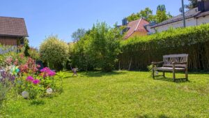 Weite Rasenfläche mit Sitzbank im Garten des Grundstücks in Forstenried im Sommer