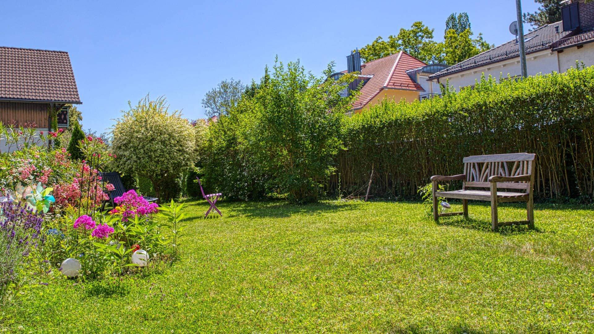 Weite Rasenfläche mit Sitzbank im Garten des Grundstücks in Forstenried im Sommer