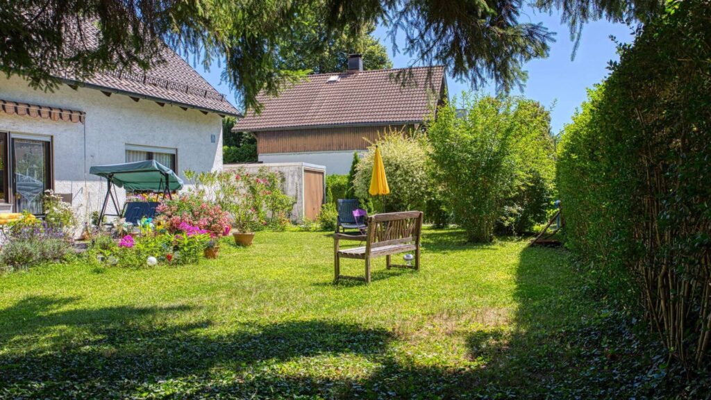 Sommerlicher Garten des Grundstücks in Forstenried mit Sitzbank, Blumenbeet und Sonnenschirm