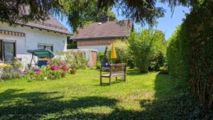 Sommerlicher Garten des Grundstücks in Forstenried mit Sitzbank, Blumenbeet und Sonnenschirm